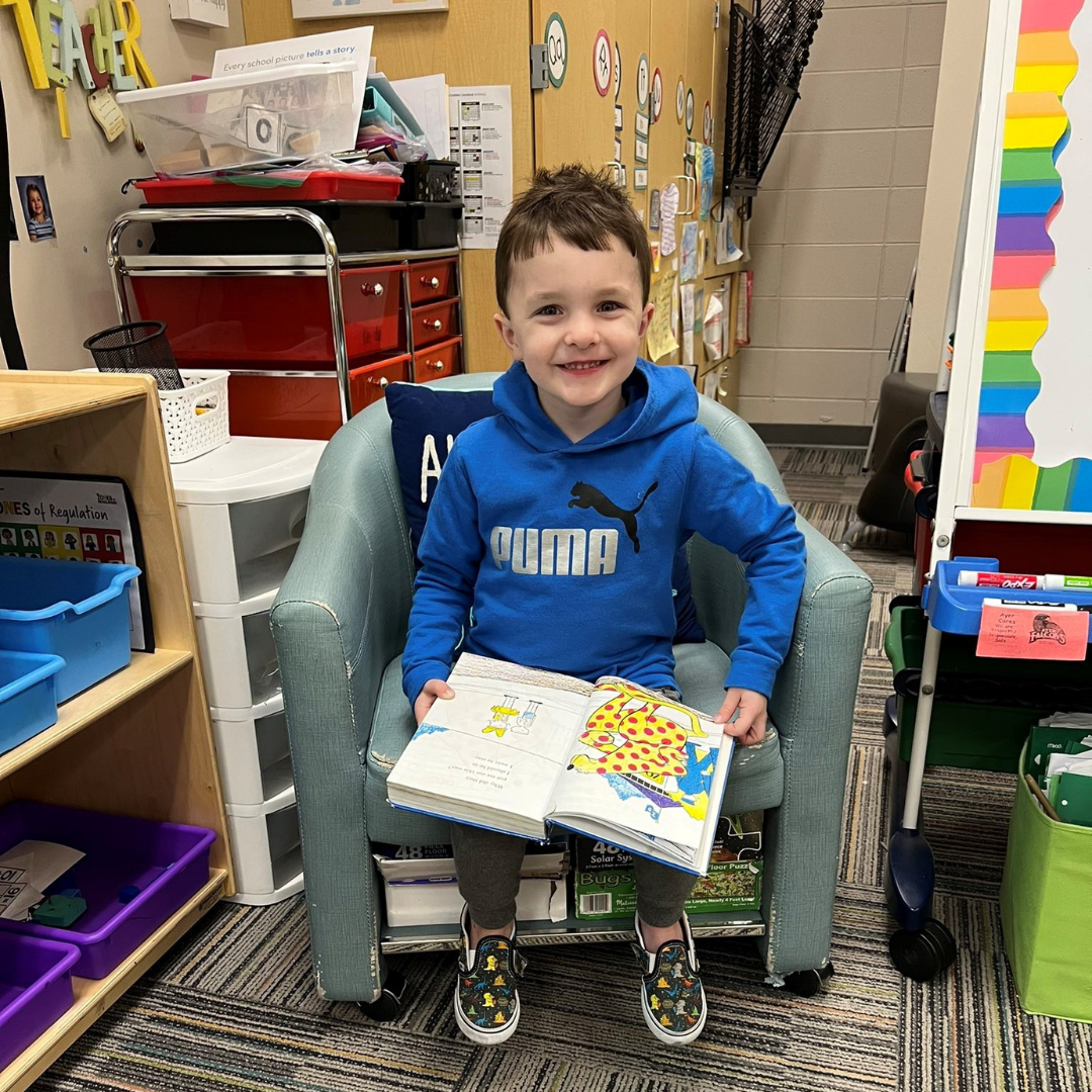 Kindergarten student smiles while holding a book